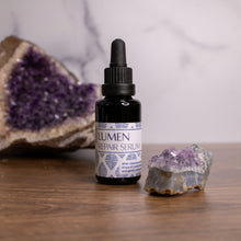 Lumen Repair Serum surrounded by amethyst crystals on a wooden surface