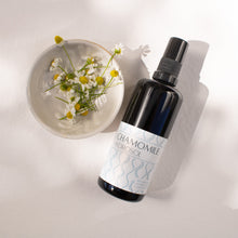 Chamomile Hydrosol on a white background with a small dish of fresh chamomile flowers