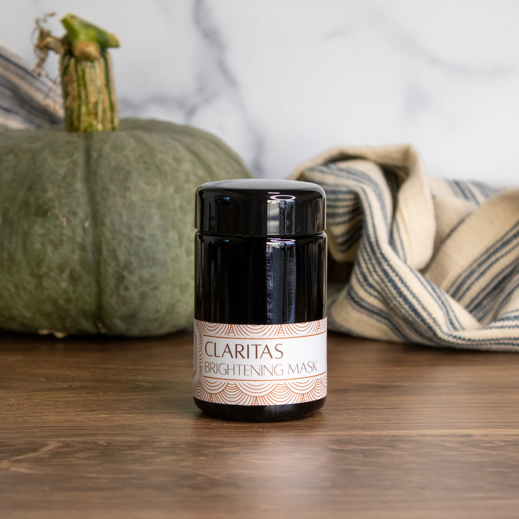 Claritas Brightening Mask with a green pumpkin and striped linens in the background