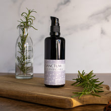 Bottle of Sanctum Cleansing Milk with a few sprigs of rosemary on a wooden surface