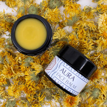 A top down photo of two jars of Aura Face Balm, one is open to show the color of the balm and the other shows the jar head on.