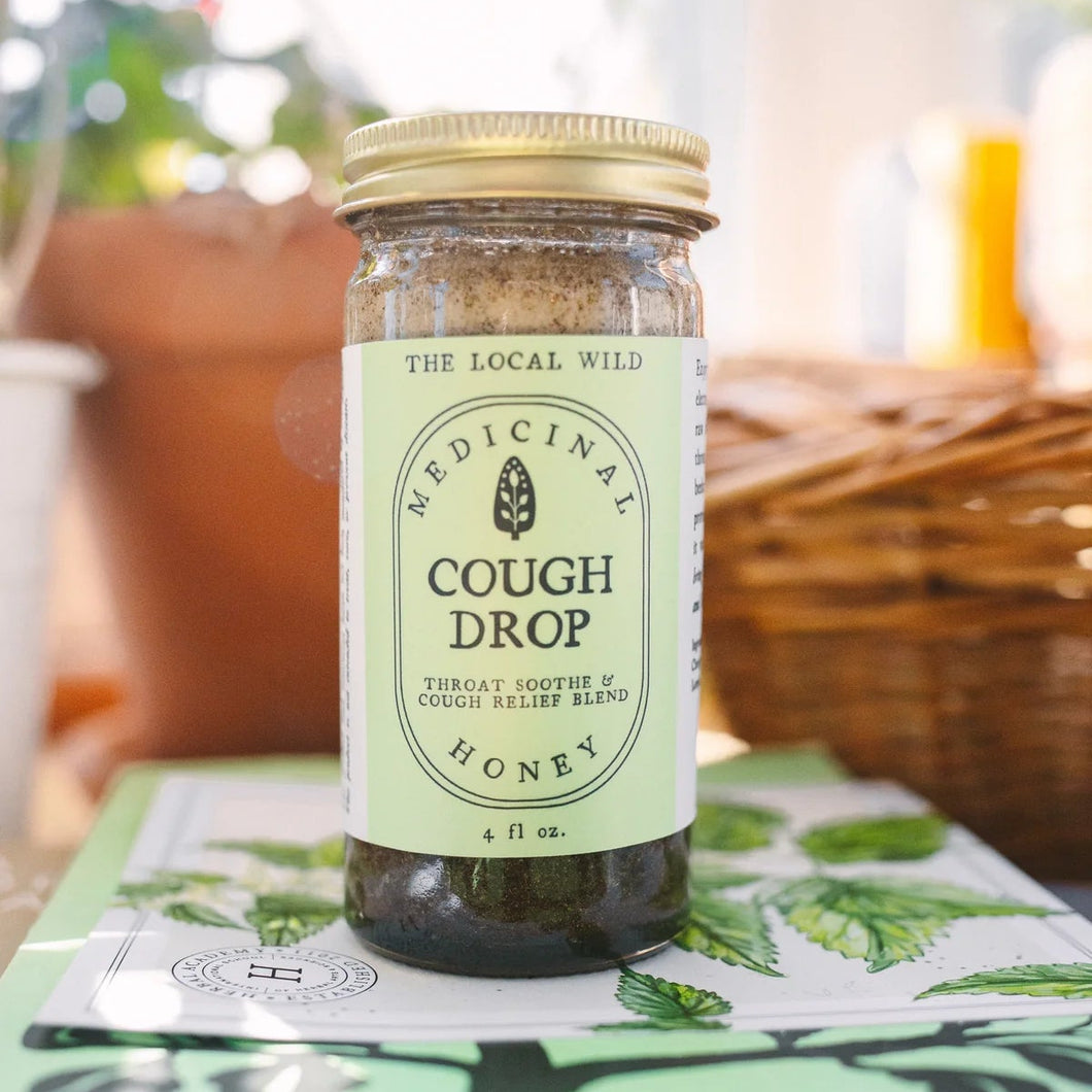 Jar of 'The Local Wild' cough drop honey on a table with a blurred background