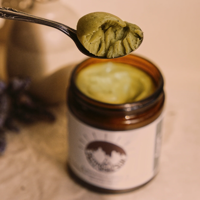 Spoonful of ghee above a jar of the same ghee on a neutral background