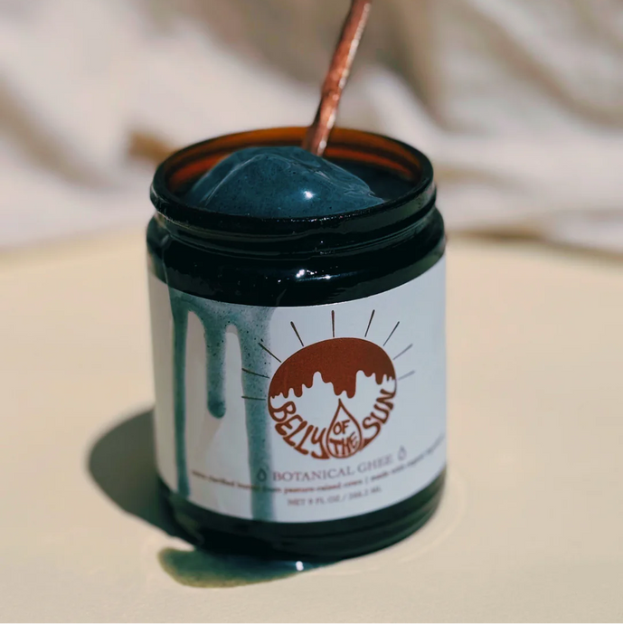 Jar of blue ghee with a spoonful being taken, against a neutral background