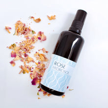 Rose Hydrosol on a white background surrounded by dried rose petals