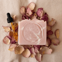 pink bar of soap on rose petals with a dropper of oil