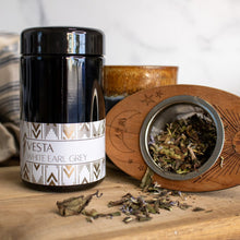 black jar of tea with a tea strainer next to it filled with loose leaf tea